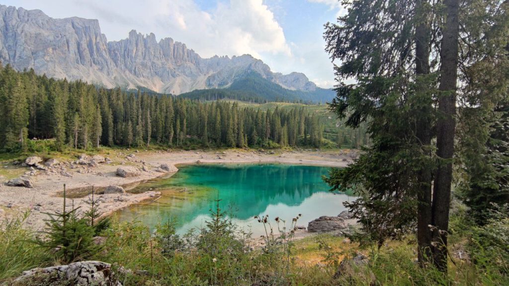 Der Kalterer See in den Dolomiten lleuchtet grün, im Hintergrund sind Berge zu sehen.